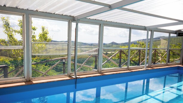 An indoor swimming pool with a view of a vineyard and hills.
