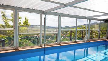 An indoor swimming pool with a view of a vineyard and hills.