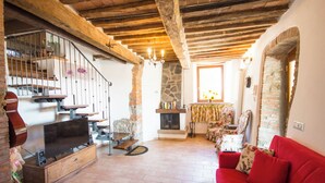 A cozy living room with a fireplace, wooden beams, a red sofa, and a television on a wooden cabinet.