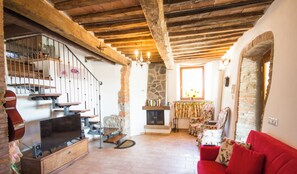 Uma sala de estar acolhedora com lareira, vigas de madeira, um sofá vermelho e uma televisão sobre um armário de madeira.