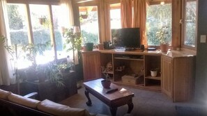 A cozy living room with a sofa, a coffee table, and a TV on a wooden cabinet. There are several potted plants around the room. - Los Maitenes Bariloche (San Carlos de Bariloche)