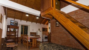 A rustic interior with a wooden staircase, a dining area with a table and chairs, a kitchen with a refrigerator and oven, and a cozy seating area. - Los Maitenes Bariloche (San Carlos de Bariloche)