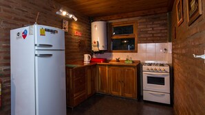 A kitchen with a refrigerator, stove, wooden cabinets, and a window. - Los Maitenes Bariloche (San Carlos de Bariloche)