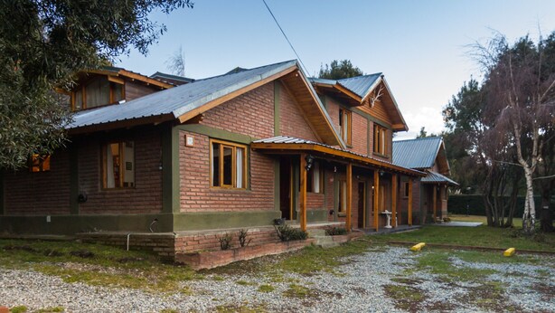 A two-story log cabin with a metal roof, a front porch, and a gravel driveway. - Los Maitenes Bariloche (San Carlos de Bariloche)