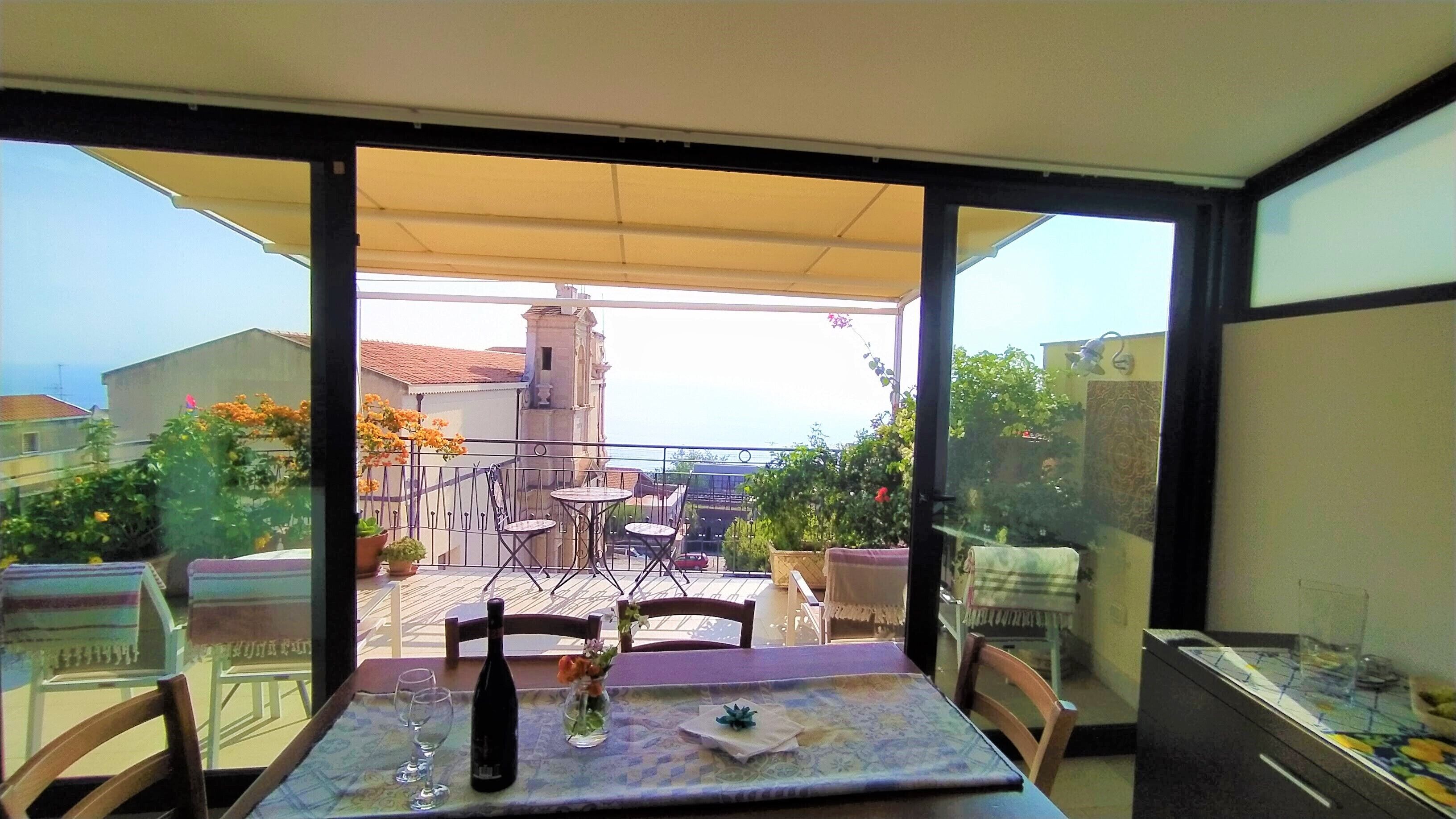 Ein Balkon mit einem Tisch für zwei Personen, einer Weinflasche und einer Blumenvase.