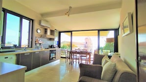 A modern kitchen with a dining area, large windows, and a view of the outside.