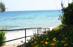 A coastal view with a beach, a person walking on the beach, and a railing with yellow flowers. - Villa Lavanda- 300sqm (11 guests) 120 seconds from the sea (Santa Margherita di Pula)