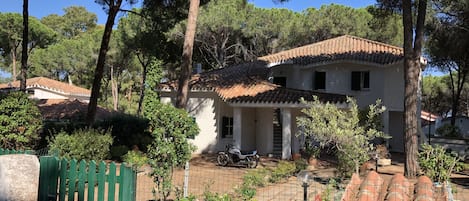 Una casa tradicional con techo de tejas, rodeada de árboles y un jardín vallado.
