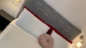 A neatly made bed with white linens, a red headboard, and a single pink pillow. There are two folded towels with brown ribbons on the bed. - Rome: Central apartment, in the heart of Rome (Roma)
