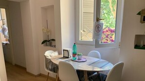 A dining area with a round table, four white chairs, a potted plant, a bottle of water, and a window with a view of greenery. - Rome: Central apartment, in the heart of Rome (Roma)