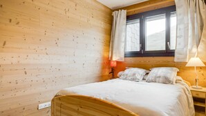 Une pièce en bois avec un lit, une fenêtre avec des rideaux et une table de chevet avec une lampe.