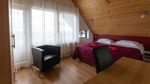 A bedroom with a wooden ceiling, a bed with a red bedspread, a black chair, and a wooden table. - Guesthouse Dalbaer (Hrunamannahreppur)