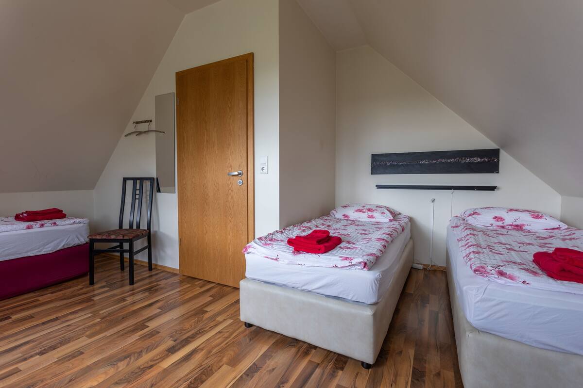 Una habitación con dos camas, piso de madera, una puerta y un estante fijado a la pared.
