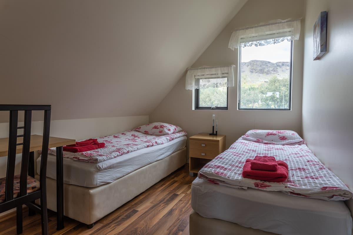 Un dormitorio con dos camas, una mesa de madera y una ventana con vistas a árboles y montañas.
