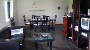 A living room with a dining table, chairs, a sofa, a coffee table, and a TV stand with a television. - Guesthouse Dalbaer (Hrunamannahreppur)