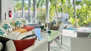 A modern outdoor living area with a glass table, white sofas, and a pool in the background. - Residence Adam & Eve (Orient Bay)