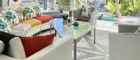 Un espace de vie extérieur moderne avec une table en verre, des canapés blancs et une piscine en arrière-plan.