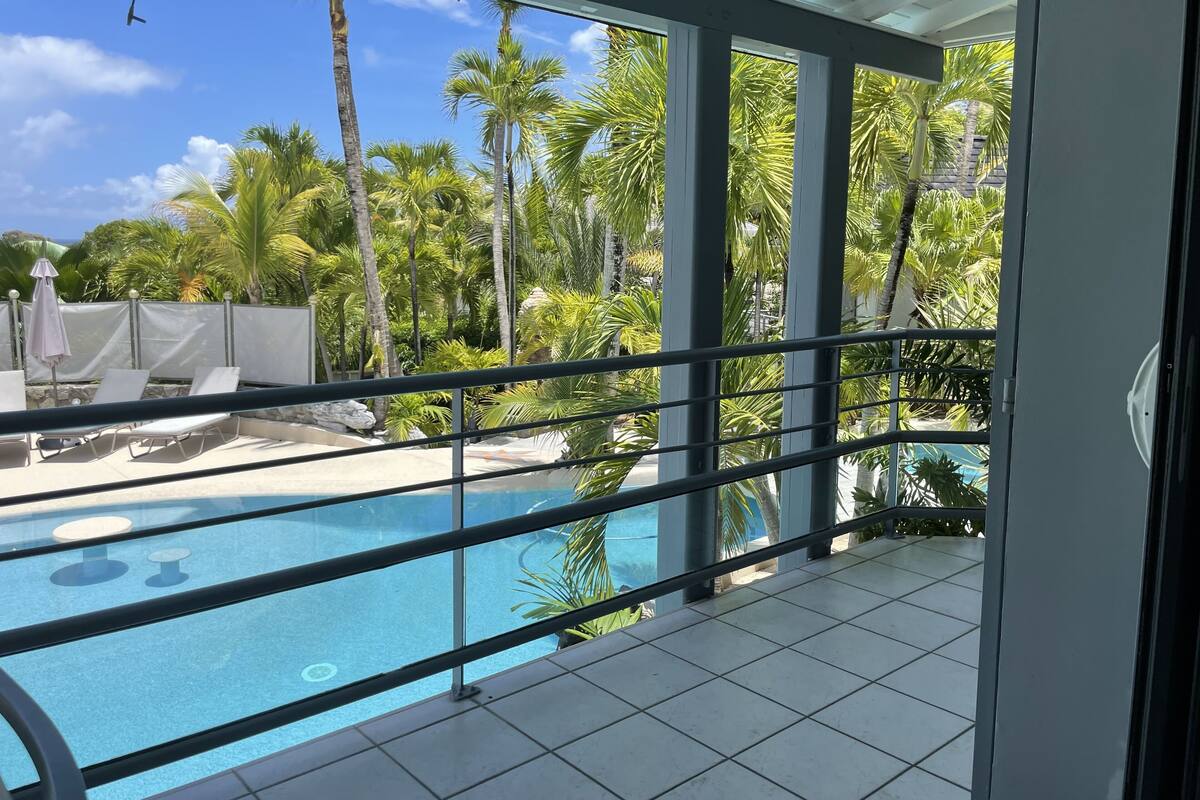 A pool area with clear blue water, surrounded by palm trees and a tiled floor.