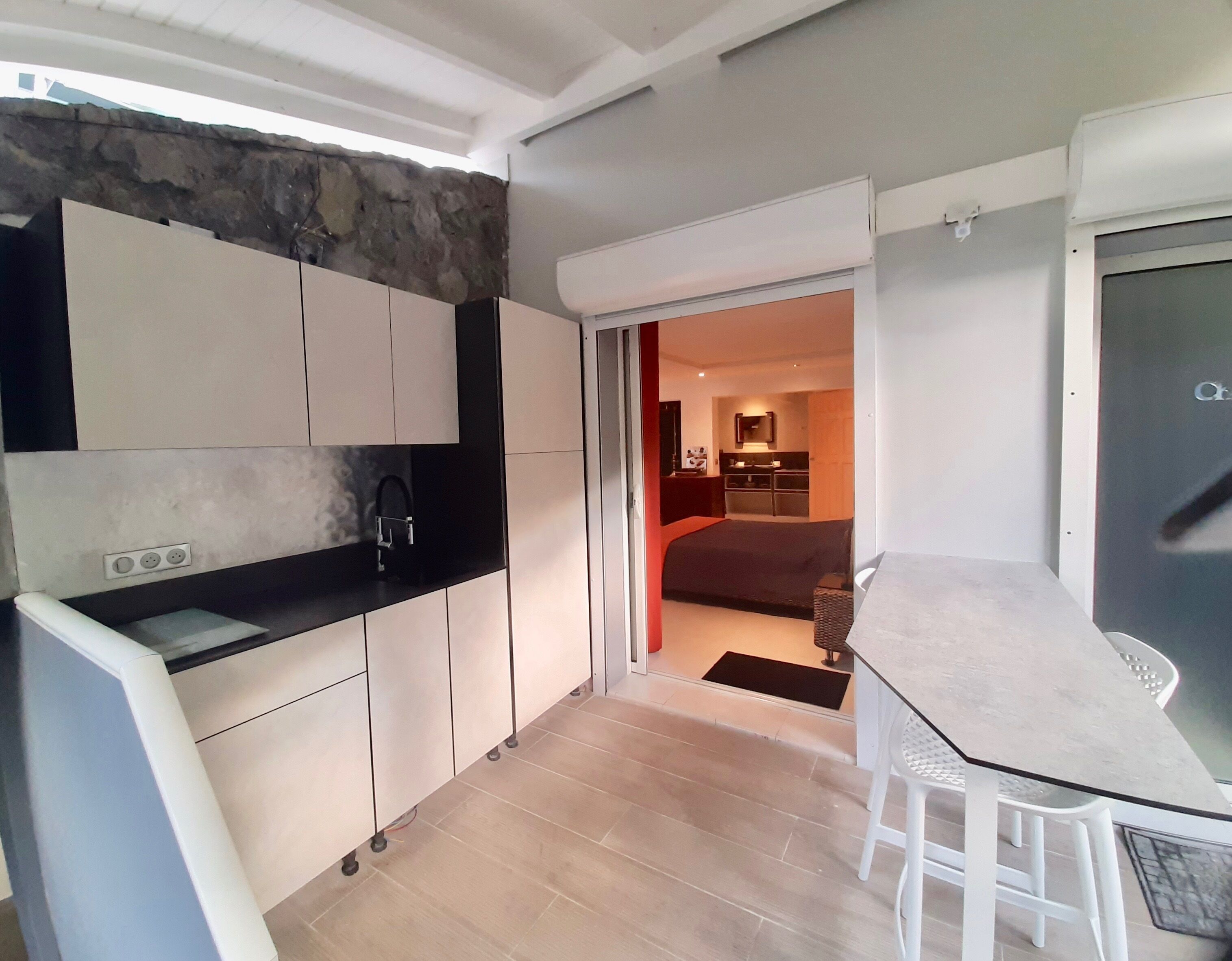 A compact kitchen with a stone accent wall, a dining area with a table and chairs, and a view into a bedroom.