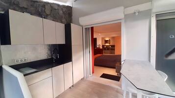 A compact kitchen with a stone accent wall, a dining area with a table and chairs, and a view into a bedroom.