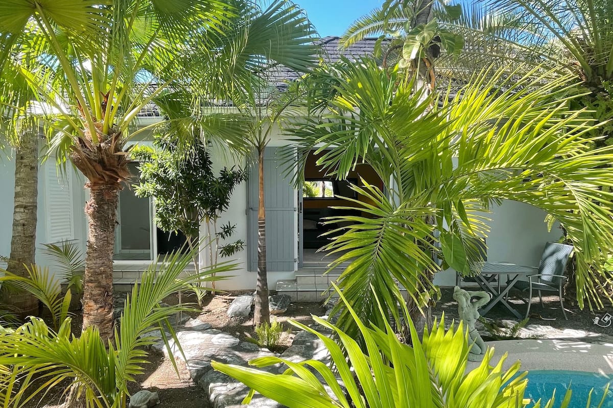 A poolside area with palm trees, a stone pathway, and a building with a white exterior and a covered patio.