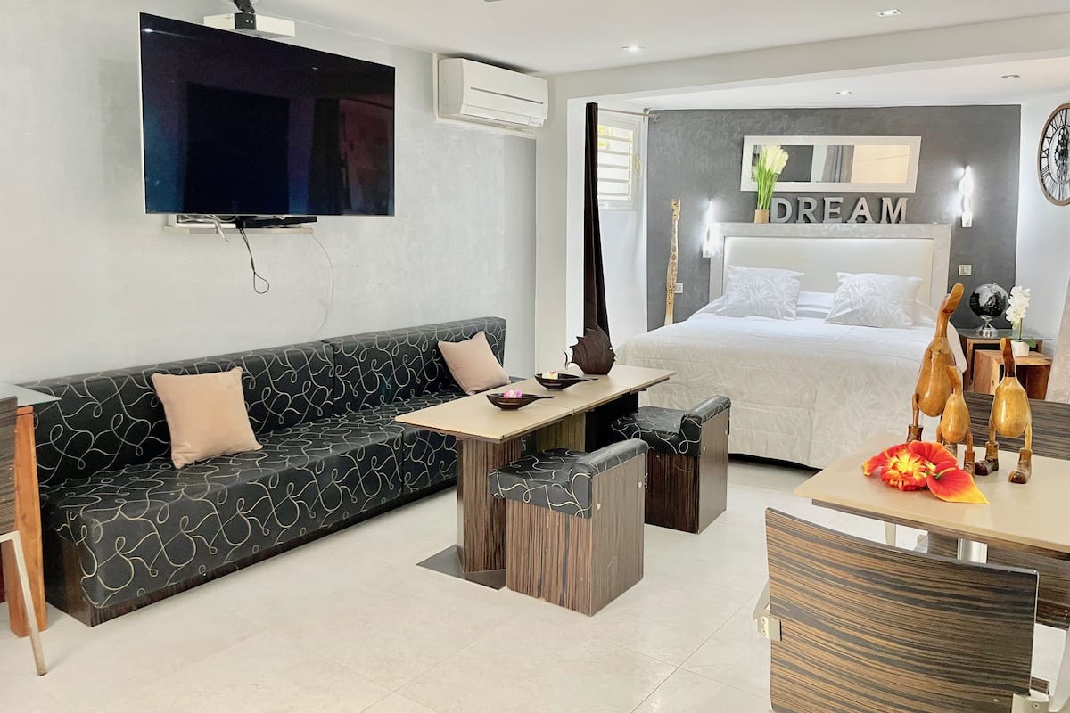 A modern hotel room with a sofa, a small table, a bed, and a TV mounted on the wall.
