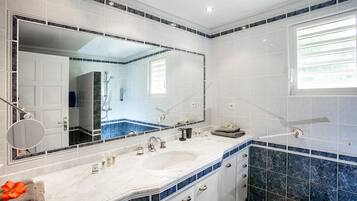 Um banheiro com um espelho grande, azulejos brancos e azuis, uma pia e uma janela.