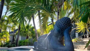 A statue of a reclining figure by a pool, surrounded by palm trees and a building with a balcony. - Residence Adam & Eve (Orient Bay)