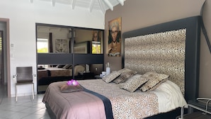 A bedroom with a large bed, a chair, a mirror, and artwork on the walls. - Residence Adam & Eve (Orient Bay)