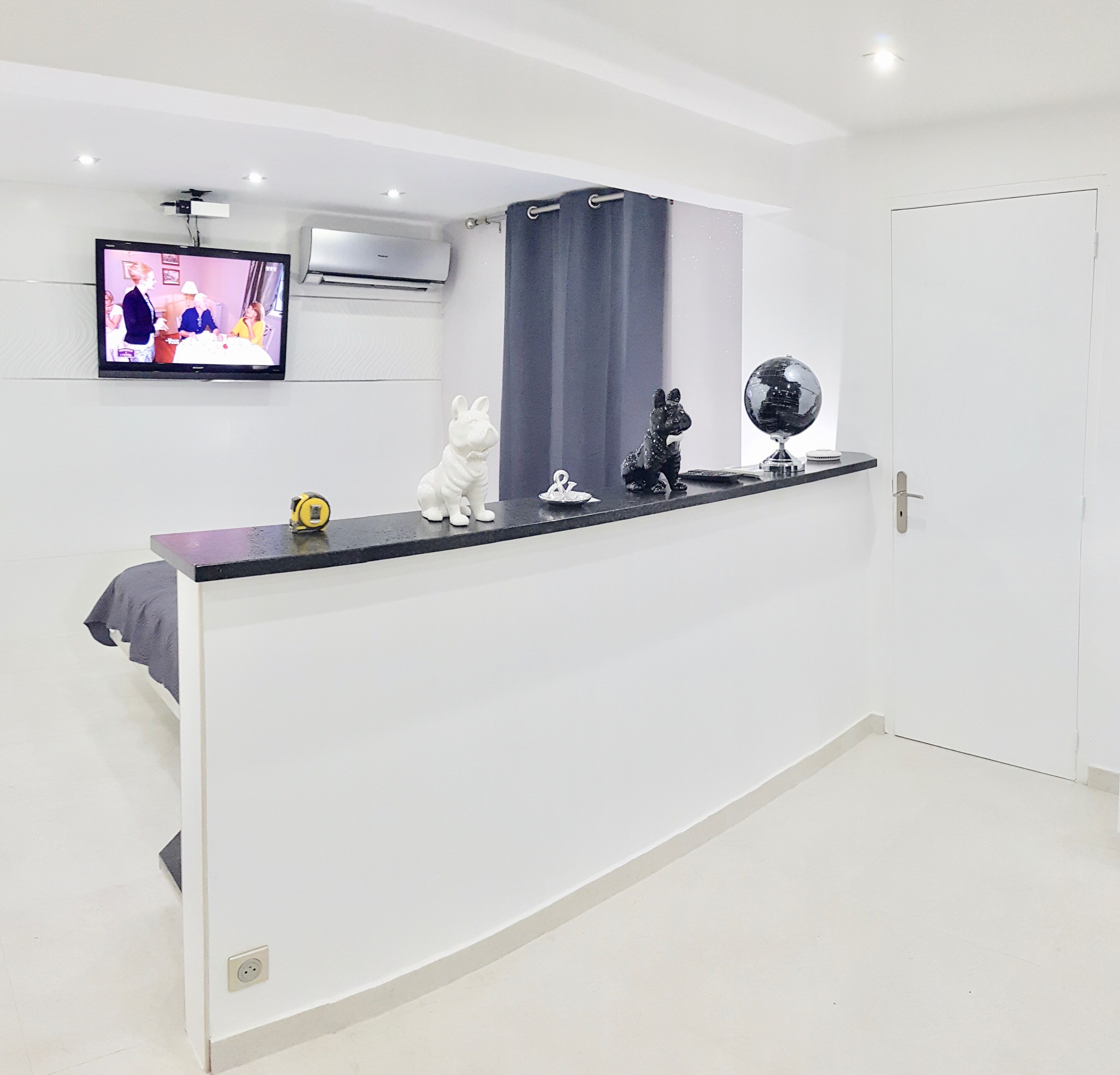 A modern room with a white wall, a black counter, a TV mounted above it, and a door to the right.