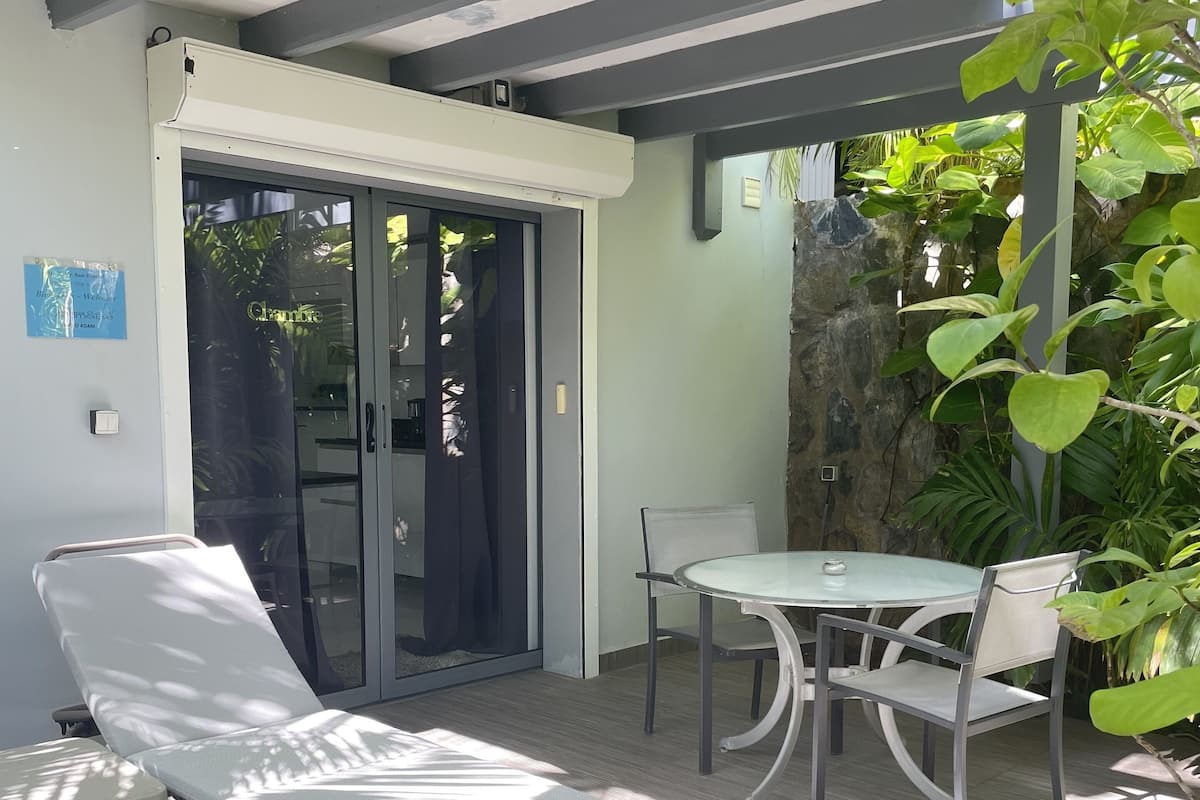 A sunlit patio with a lounge chair, a table, and chairs.