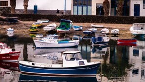 Un puerto deportivo con varias embarcaciones amarradas, una superficie de agua tranquila y un edificio con puertas azules al fondo.