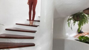 Une personne se tient sur un escalier, les murs sont blancs et il y a une plante dans le coin.