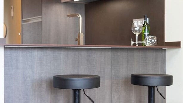 Un área de cocina moderna con una barra, dos taburetes, y una copa y una botella de vino sobre la barra.