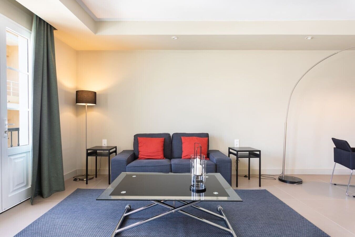 Una sala de estar moderna con una mesa de centro de vidrio, un sofá con cojines rojos, una lámpara de pie y una silla negra.