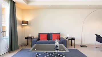 Una sala de estar moderna con una mesa de centro de vidrio, un sofá con cojines rojos, una lámpara de pie y una silla negra.