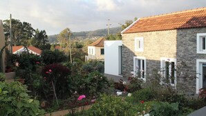 A stone building with a tiled roof, surrounded by a garden with various plants and flowers.