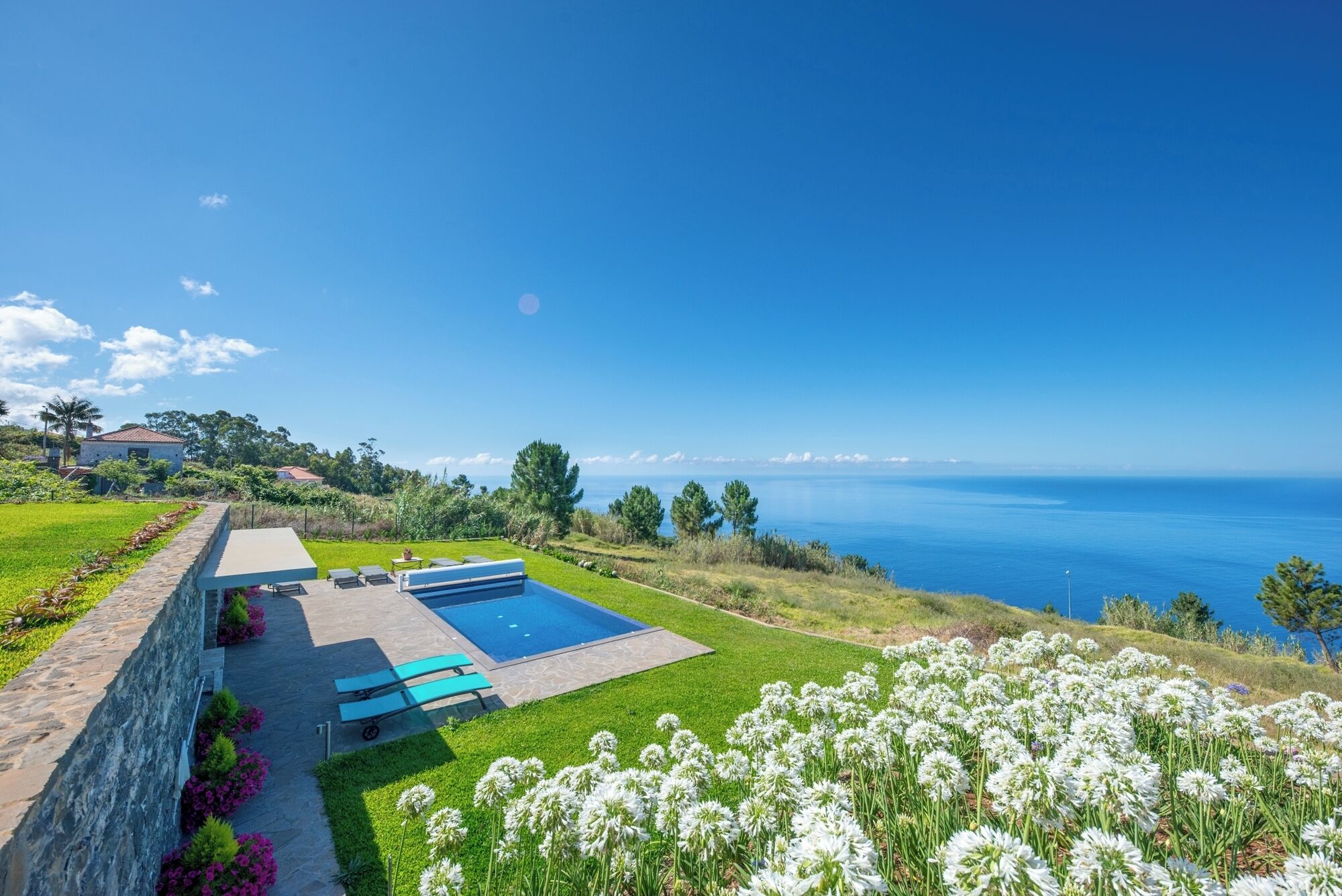 Une maison moderne avec une piscine, un mur en pierre et une vue sur la mer.
