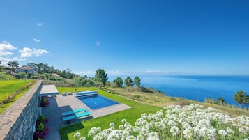 Une maison moderne avec une piscine, un mur en pierre et une vue sur la mer.