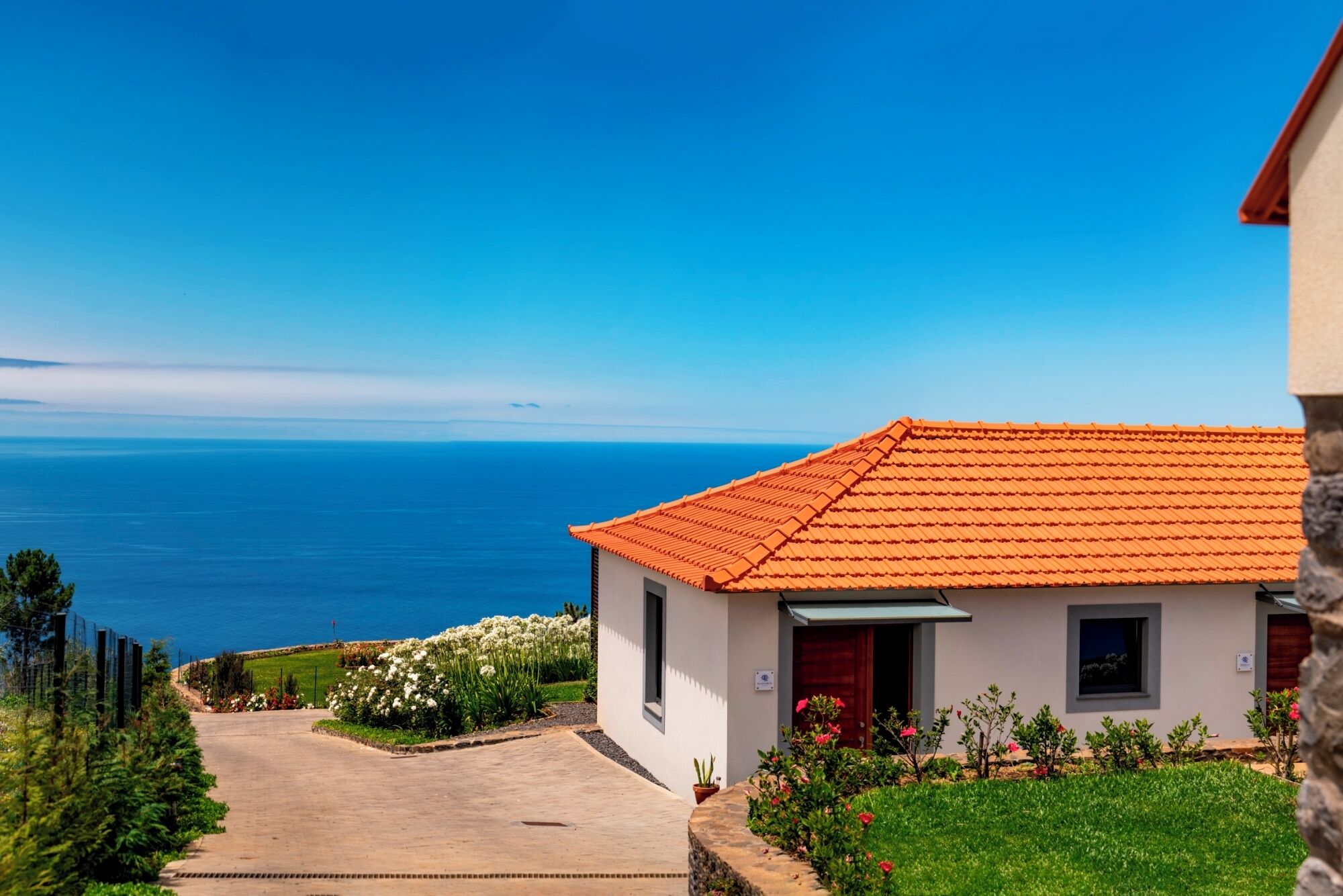 Un bâtiment situé sur la côte, doté d’un toit recouvert de tuiles, d’une allée pavée et offrant une vue sur la mer.