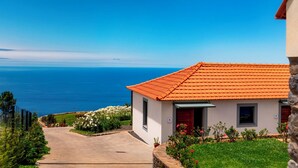 A coastal building with a tiled roof, a paved driveway, and a view of the sea.