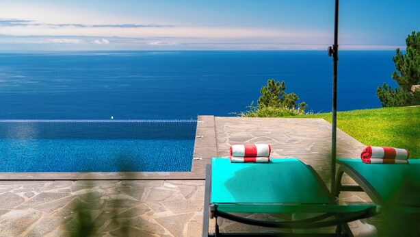 A pool with a view of the sea, a green lounge chair, and an orange umbrella.