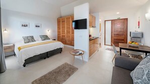A modern hotel room with a bed, a TV, a dining area, and a kitchen.