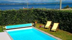 Une piscine avec vue sur la mer, deux chaises longues et une haie.