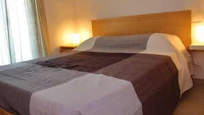 A neatly made bed with a wooden headboard, two bedside lamps, and a window with curtains.