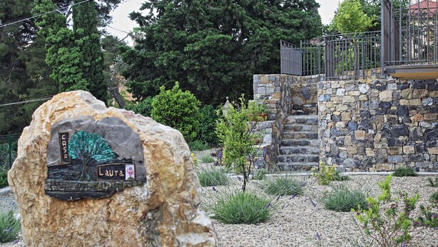 A stone wall with a plaque, a small tree, and a gravel path.