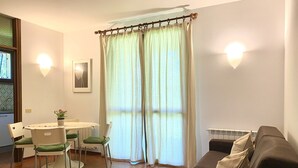 A living room with a brown sofa, a dining table with chairs, and a window with curtains.
