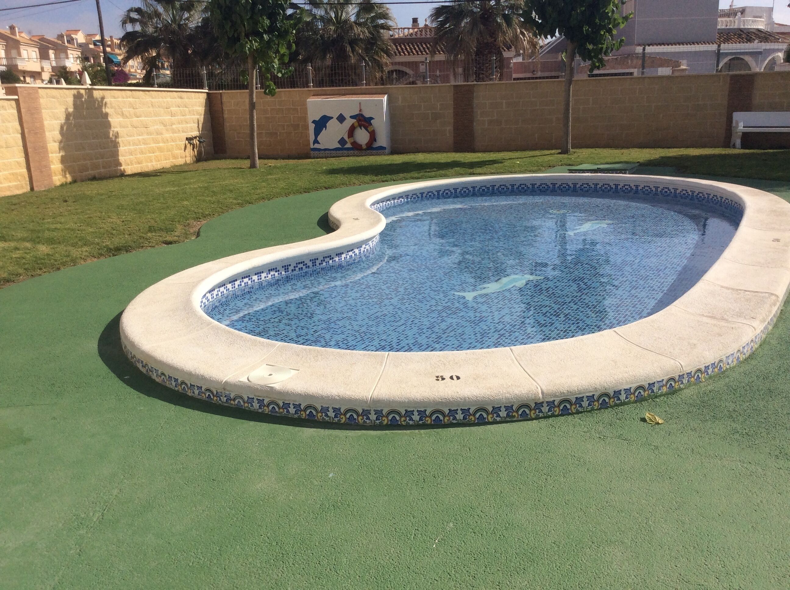 A swimming pool with a blue mosaic tile interior, surrounded by a green artificial turf area.