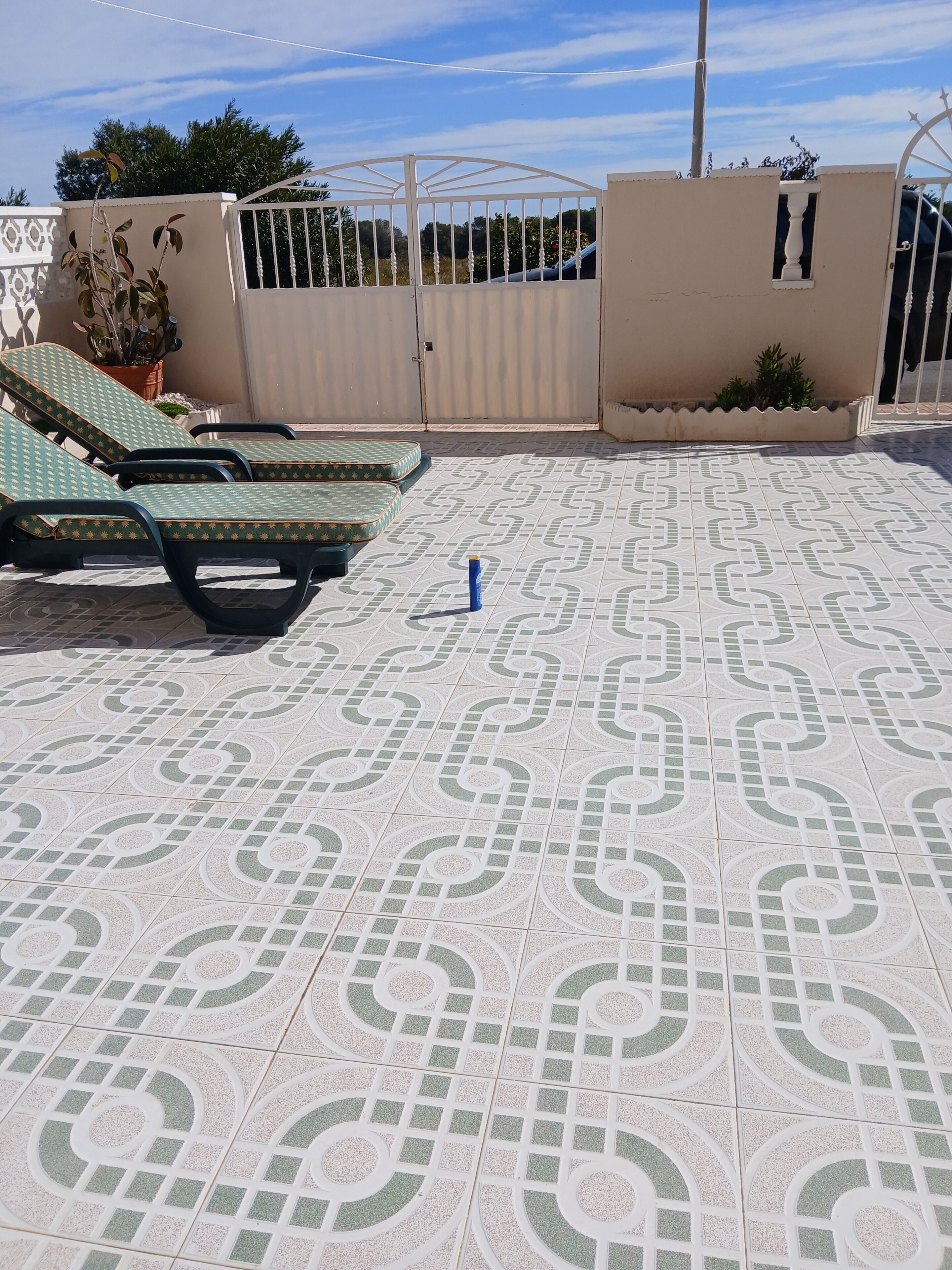 A rooftop terrace with patterned tiles, a gate, and lounge chairs.