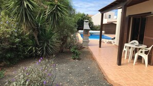 Eine Terrasse mit Pool, umgeben von viel Grün und einem kleinen Tisch mit Stühlen.